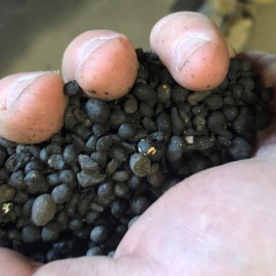 A close-up photo of a hand holding granules of black compost